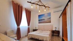 Une chambre à coucher comprenant un lit, un bureau, une chaise, un tableau représentant une plage et un lustre original.