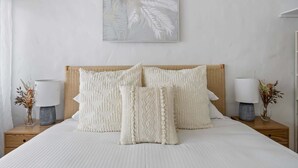 A neatly made bed with white bedding and decorative pillows, flanked by two bedside tables with lamps and small vases.