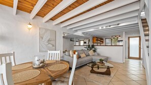 A spacious living area with a wooden ceiling, a dining table with chairs, a sofa, and a coffee table.