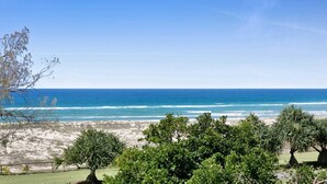 Blick auf die Küste mit blauem Himmel, sandigem Strand und üppiger Vegetation im Vordergrund.