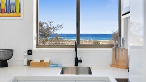 Eine Küche mit großem Fenster zum Strandblick, einem Edelstahl-Spülbecken und einem Holzer Schneidebrett.