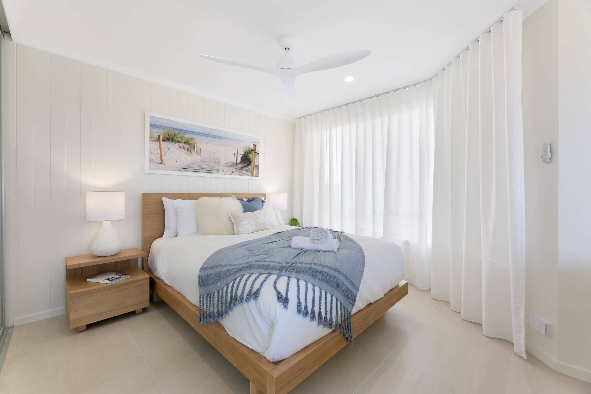 Une chambre à coucher avec un lit, une table de chevet, un ventilateur de plafond, un tableau et des rideaux en voile.