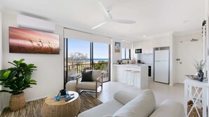 Ein modernes Wohnzimmer mit einer Couch, einem runden Couchtisch und Blick auf den Strand durch große Fenster.