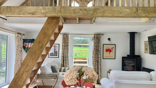A cozy room with a wooden staircase, a dining table with chairs, a sofa, and a fireplace.
