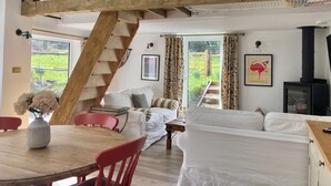 A cozy room with a wooden staircase, a sofa, a table with a vase, and a fireplace.