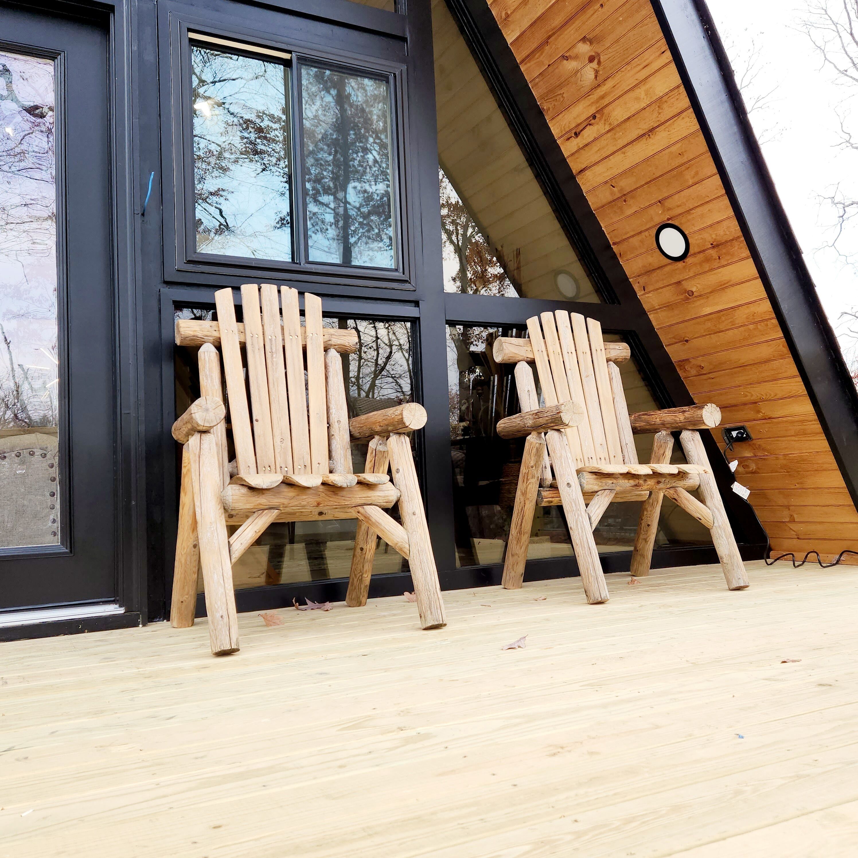 Two wooden Adirondack chairs on a wooden deck in front of a building with large windows and a sloped roof.