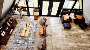 Ein gemütlicher Raum mit hohen Decken und einem großen Fenster mit Seeblick, ausgestattet mit einer Couch, Sesseln und einem Couchtisch.