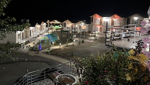 A nighttime view of a resort with multiple bungalow-style accommodations, a central open area with a covered seating area, and a pool. - Resort Prakriti Unwind (Chakrata)