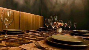 A dining table set with plates, glasses, and cutlery, with a vase of flowers and a cushioned bench in the background.