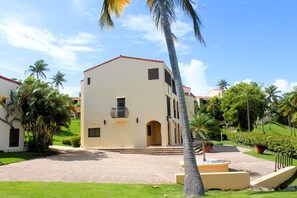A building with a red roof, white walls, and a paved courtyard with palm trees. - 2Bed/2Bath at the Tennis Village at Palmas del Mar (Humacao)