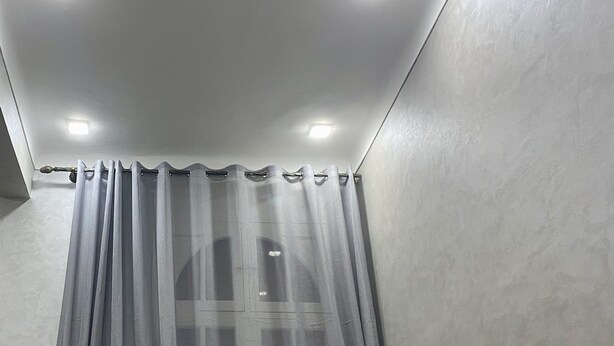 Un baño con cortina de ducha, techo con luces empotradas y una pared lisa.