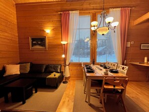 En mysig stuga med träpanel på väggarna, ett matbord för fyra personer, en soffa och en kristallkrona.