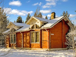 A wooden cabin with a gabled roof, large windows, and a chimney.