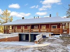 En tvåvånings timmerstuga med en inglasad veranda och ett snötäckt tak.