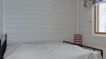 Ein Zimmer mit einem Einzelbett, einem Fenster mit Blumenvorhang und einem roten Sessel.