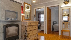 Een kamer met een open haard, een houten dressoir en een spiegel. Er is een deur die naar een andere kamer leidt.
