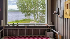 Een kamer met een groot raam met uitzicht op een meer, een geruit vloerkleed en een sauna-cabine op de vensterbank.