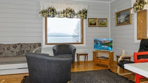 Een woonkamer met een bank, twee fauteuils, een houten salontafel en een televisie. Er is een raam met uitzicht op een meer en bergen.