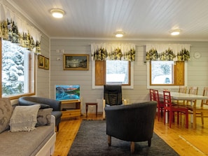 A cozy living room with a sofa, a TV, a dining table with chairs, and a fireplace. - Käpälämäki by Interhome (Ylitornio)