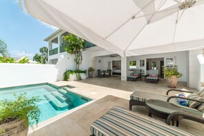 A poolside area with a covered patio, outdoor seating, and a view of the house.