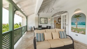 A covered outdoor seating area with a beige sofa, striped pillows, and a view of the outdoors.