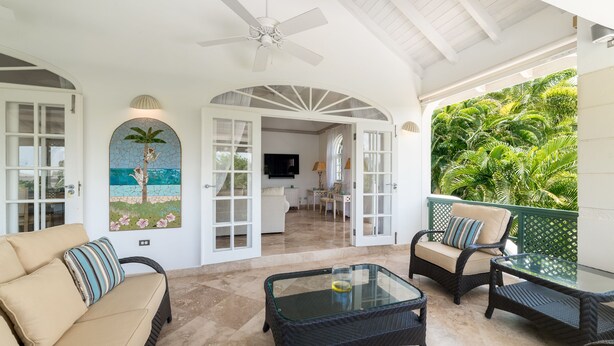 A covered outdoor seating area with wicker furniture, a glass coffee table, and a mural of a palm tree.