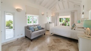 A spacious bedroom with a large bed, a sofa, and a dresser. There are windows providing natural light and a view of greenery outside.