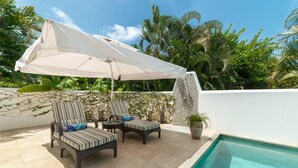 A poolside area with two striped lounge chairs, a white umbrella, and a small potted plant.