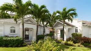 A white building with a symmetrical facade, palm trees, and a well-maintained garden.