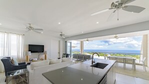 A modern living room with a large island, a sofa, and a TV. There is a balcony with a view of the ocean. - White 4 bedroom villa with amazing ocean views in a gated community in St James (Fitts Village)