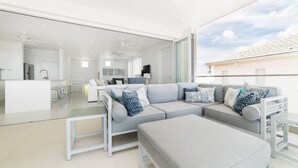A modern living room with a grey sectional sofa, a glass coffee table, and a white dining area. - White 4 bedroom villa with amazing ocean views in a gated community in St James (Fitts Village)