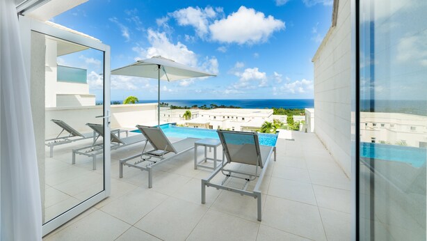 A balcony with a pool, lounge chairs, and a view of the ocean. - White 4 bedroom villa with amazing ocean views in a gated community in St James (Fitts Village)