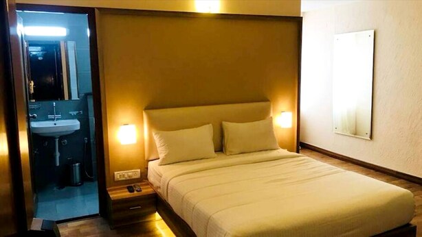 A hotel room with a bed, bedside lamps, a nightstand, a mirror, and a wall-mounted light. - PPH Living EDEN PARK HOTEL INDIRA NAGAR (Bengaluru)