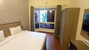 A hotel room with a large bed, a television, and a window with curtains. - PPH Living EDEN PARK HOTEL INDIRA NAGAR (Bengaluru)