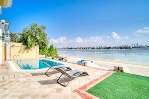 A pool area with lounge chairs, a view of the sea, and a city skyline in the background.