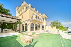 A large, two-story house with a covered patio, outdoor furniture, and a well-maintained lawn.