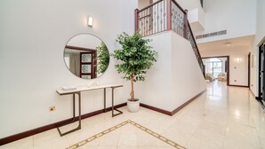 Un hall d’entrée spacieux avec un escalier, un grand miroir rond, un arbre en pot et une petite table.