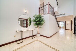 A spacious hallway with a staircase, a round mirror, a potted tree, and a small table.