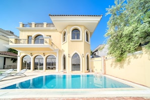 A two-story house with a swimming pool, arched windows, and a balcony.