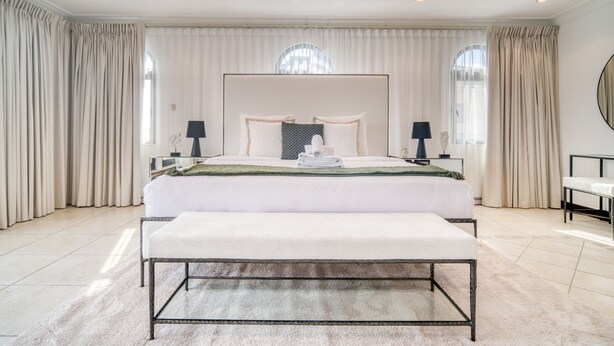 Un grand lit avec une tête de lit, des tables de chevet, un banc et un grand miroir.