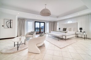 A modern hotel room with a large bed, a sofa, a coffee table, and a view of the city through the window.
