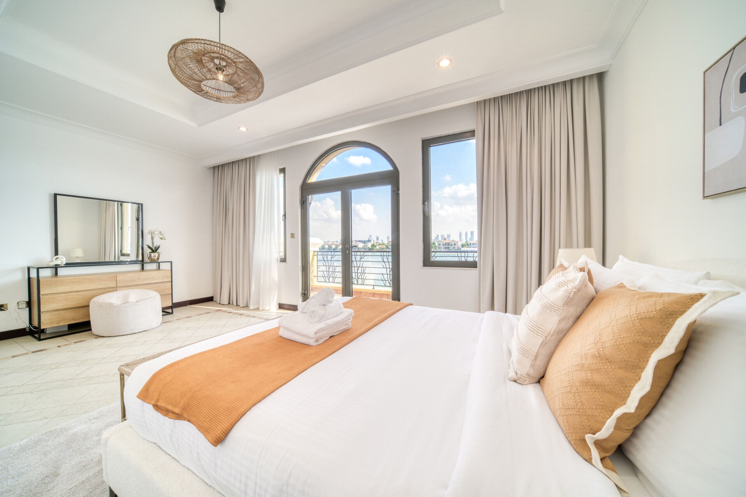 Une chambre d’hôtel avec un grand lit, une coiffeuse avec un miroir, un bureau et une vue sur la ville par les fenêtres.