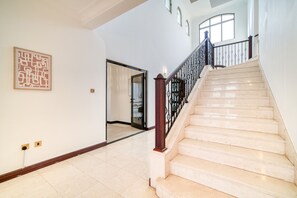 A spacious hallway with a marble staircase, a framed abstract artwork, and a door leading to another room.