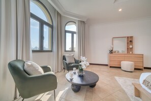Habitación de hotel moderna con un ventanal grande, una mesa de centro redonda, un sofá, una silla, un aparador y una cama.