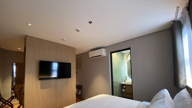 A modern hotel room with a large bed, a flat-screen TV mounted on the wall, and a bathroom visible through an open door. - Moonstar Cebu Hotel (Cebu City)
