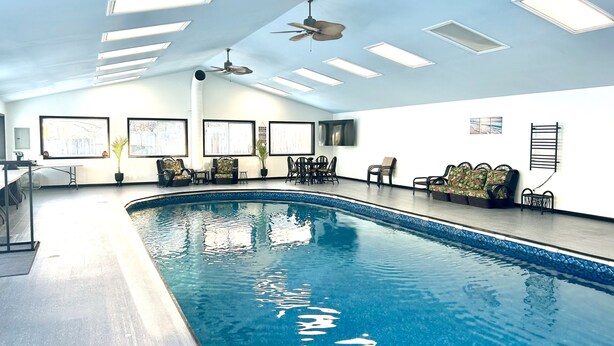Une piscine intérieure dotée de ventilateurs de plafond, d’espaces aménagés pour s’asseoir et d’œuvres d’art encadrées accrochées aux murs.