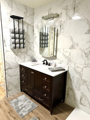 A bathroom with a marble wall, a dark wooden vanity, a sink, and a towel rack. - Family friendly, centrally located home with a pool! (Wasilla)