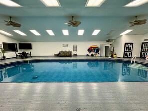 A large indoor swimming pool with ceiling fans, a seating area, and a wall with various items. - Family friendly, centrally located home with a pool! (Wasilla)