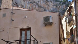 Eine enge Straße mit Gebäuden, die Balkone, Steinmauern und einen felsigen Felsvorsprung im Hintergrund aufweisen.
