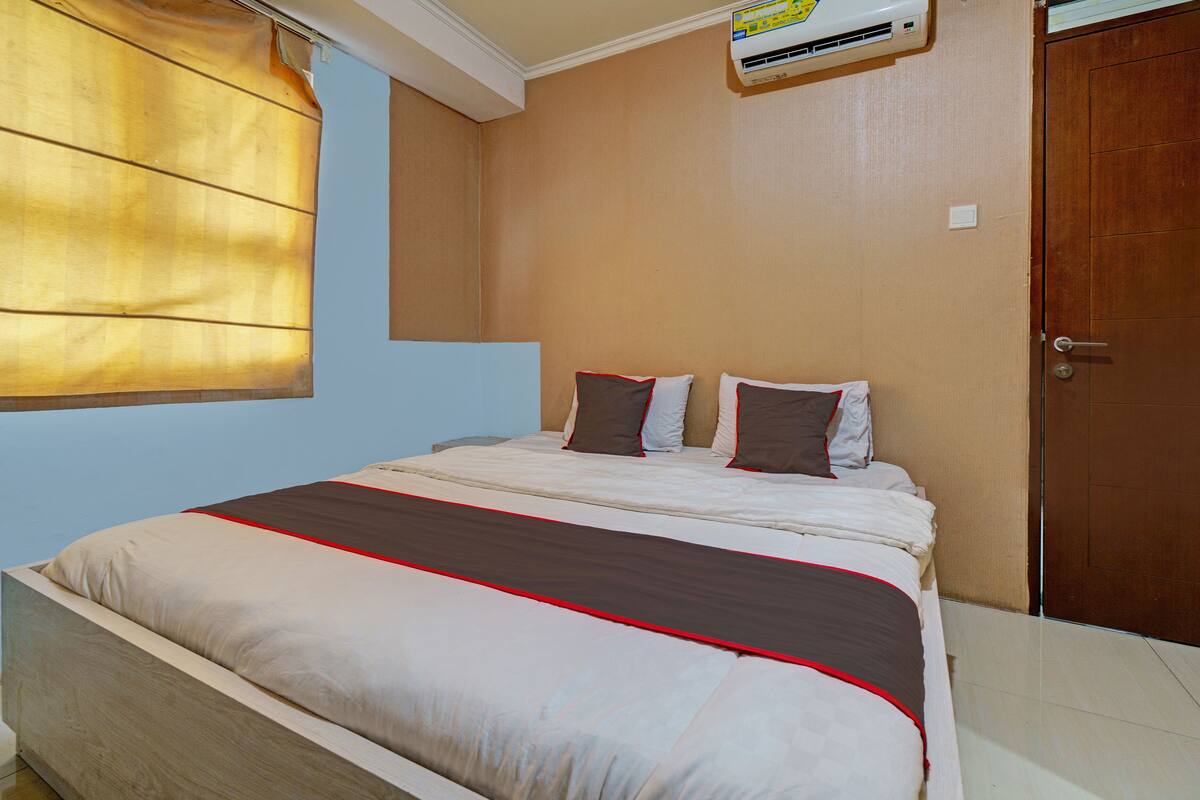 A bedroom with a bed, a window with curtains, an air conditioning unit, and a wooden door.